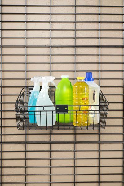 A wire basket filled with cleaning supplies is hanging on a wall.