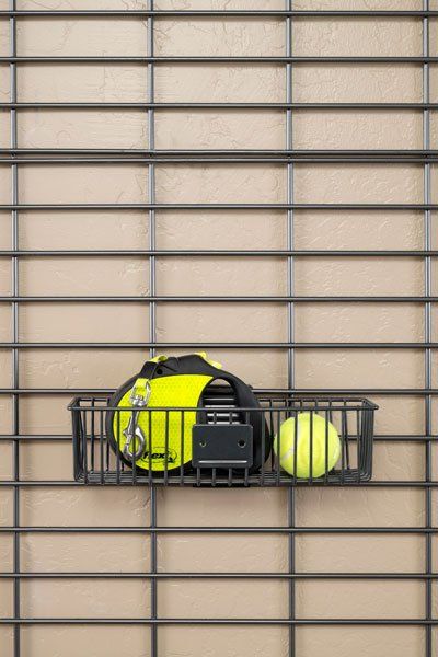 A basket filled with tennis balls is hanging on a wall.