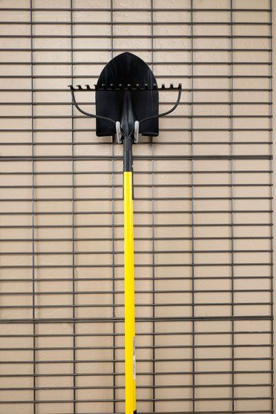 A shovel and rake are hanging on a rack on a wall.