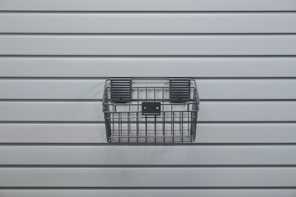 A wire basket is hanging on a slat wall.