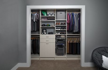 A organized reach-in closet with hanging clothes, shelves, drawers, and shoe racks set against grey walls.