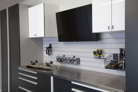 Modern garage workspace with a stainless steel countertop, black cabinets, white upper cabinets, and wall-mounted tools.