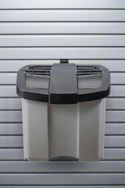 A white trash can with a black lid is hanging on a wall.