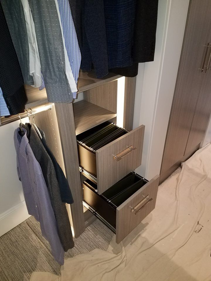 A closet with drawers open and clothes hanging on the wall.