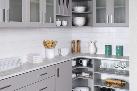 A modern kitchen with grey cabinets, white subway tile backsplash, light countertops, and open corner shelving.