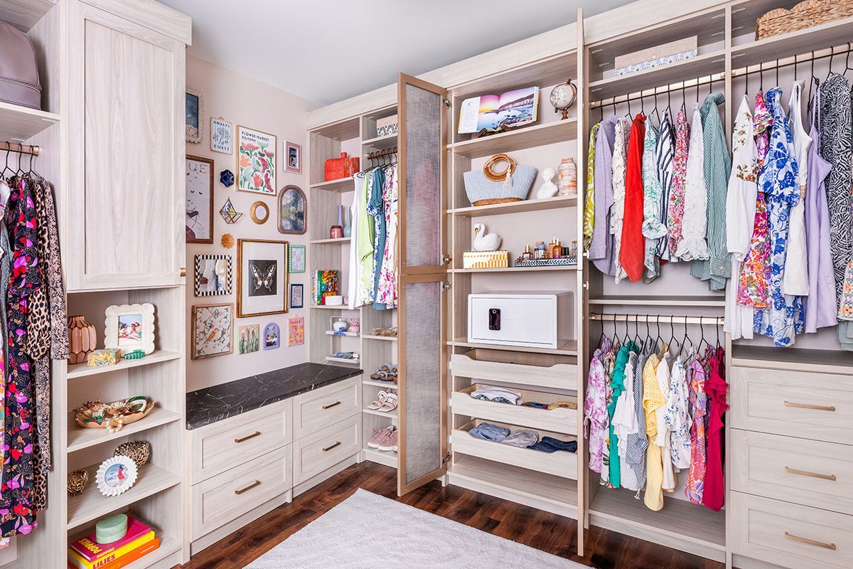 A custom organized walk-in closet with light wood shelving, hanging clothes, drawers, and a gallery wall above a bench.