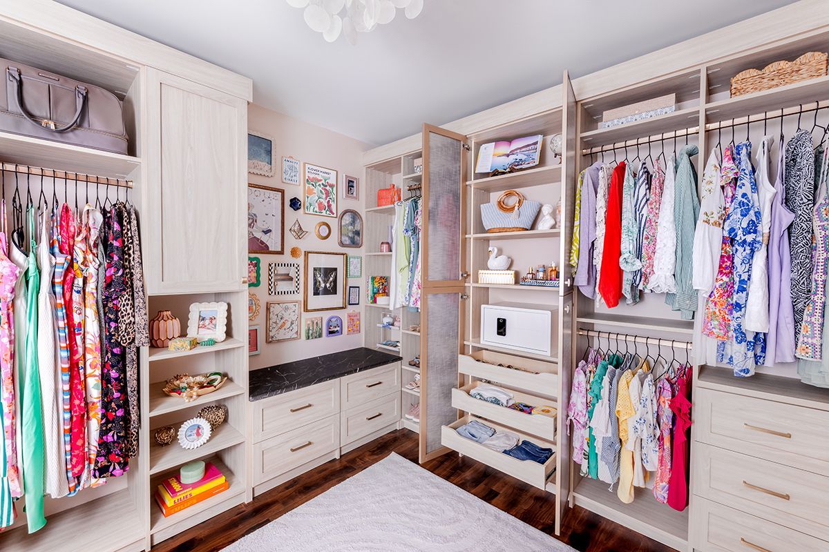 A bright, organized walk-in closet with hanging clothes, shelves, built-in drawers, and a gallery wall above a bench.