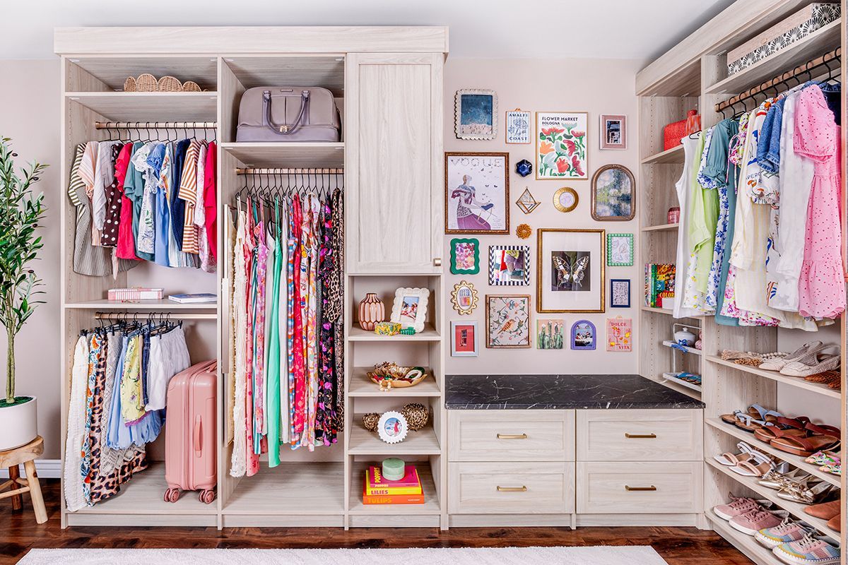 A bright, organized walk-in closet featuring hanging clothes, shelving, a built-in bench with drawers, and wall art.