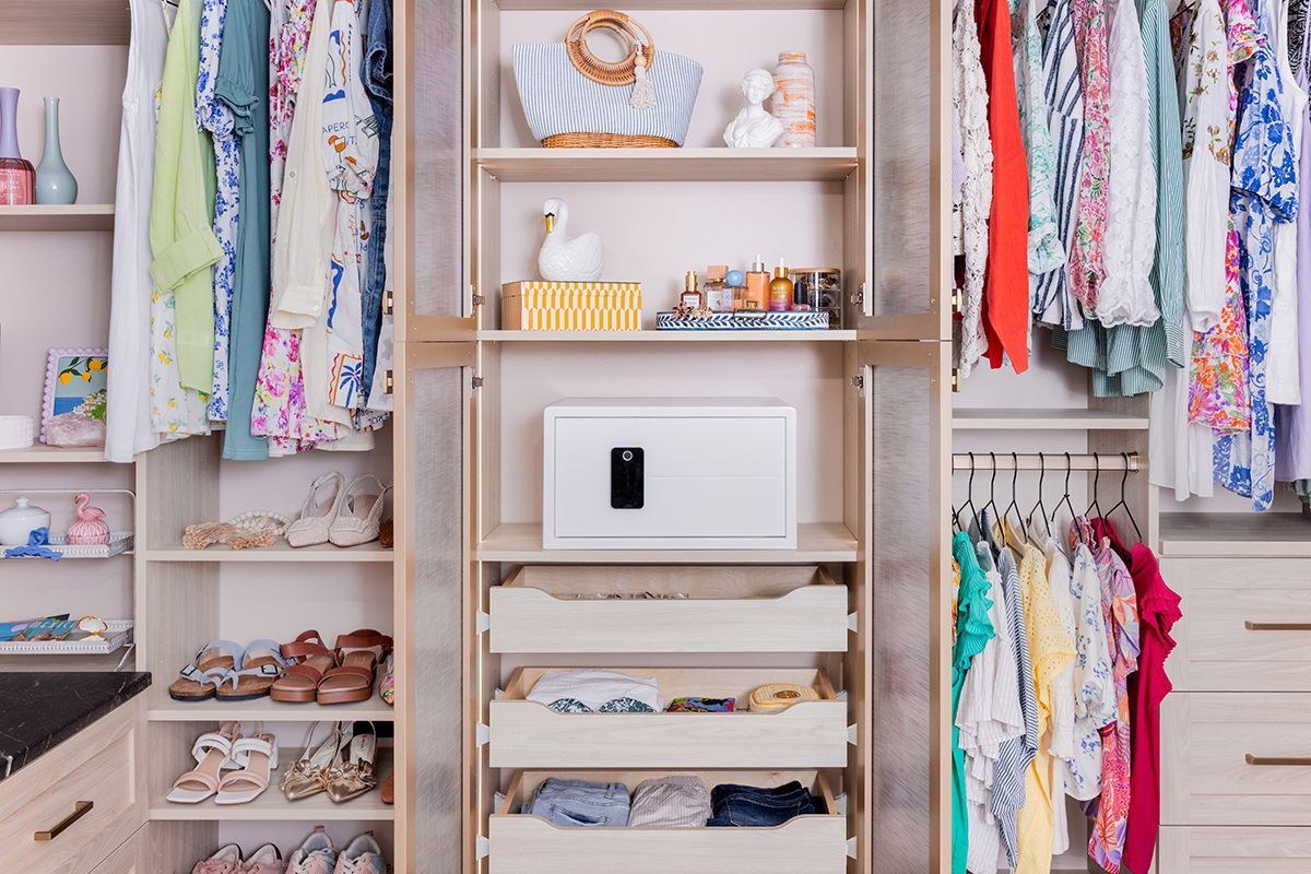 A well-organized walk-in closet featuring hanging garments, shelves filled with shoes, decor, and a central security safe.