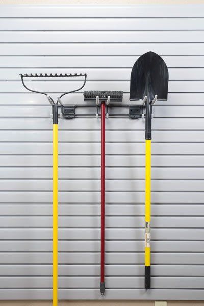 A shovel , rake , and mop are hanging on a wall.
