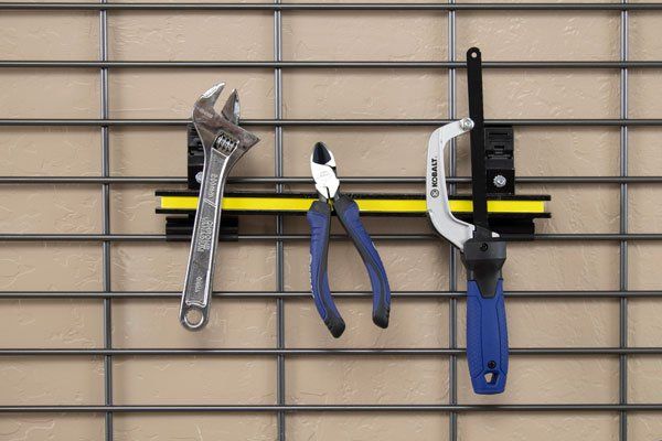 A wrench , pliers , and a saw are hanging on a wire rack.
