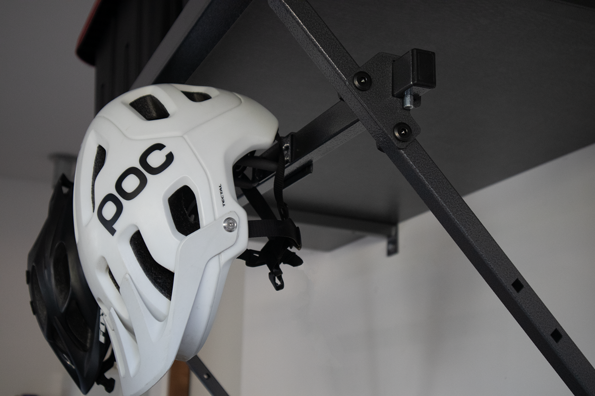 A white POC helmet and a black helmet hanging from a black metal rack attached to a wall.