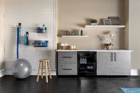 A modern home gym or utility area with cabinets, floating shelves, exercise ball, and storage accessories against a wall.