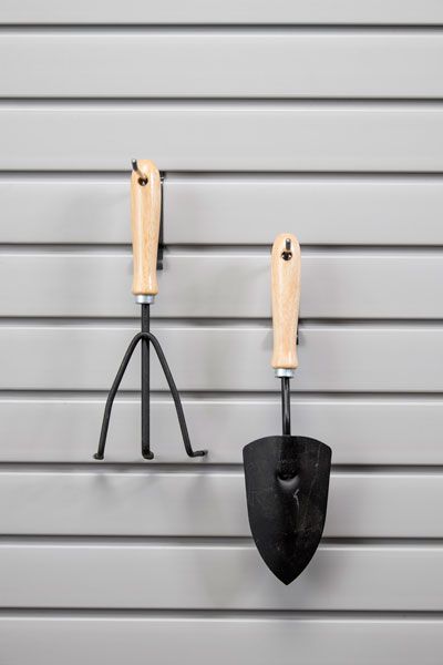 A rake and a shovel are hanging on a wall.