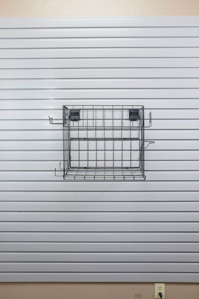 A slat wall with a wire basket attached to it.