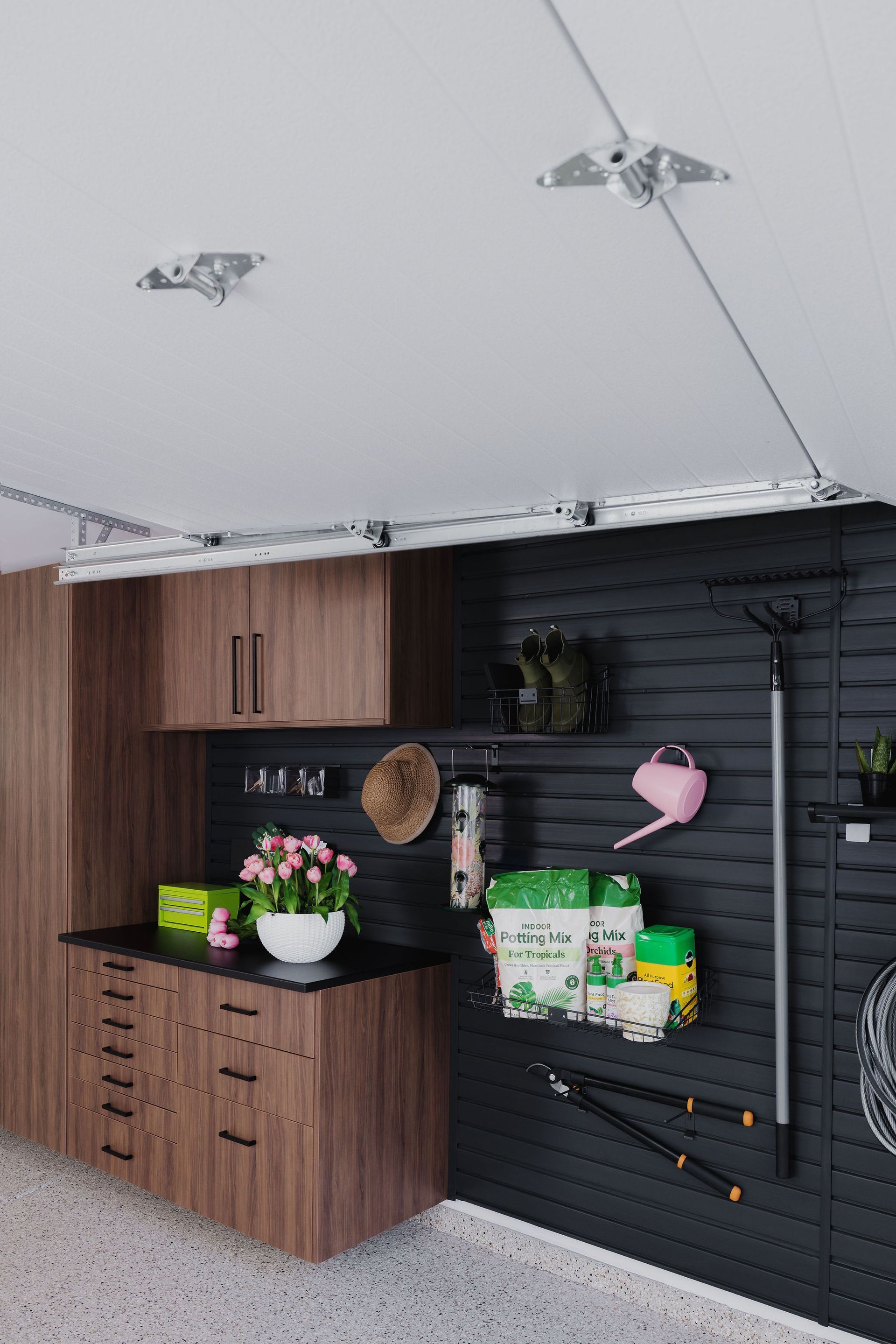 A modern garage storage wall featuring wooden cabinets, a dark slatted organization system, and various hanging garden tools.