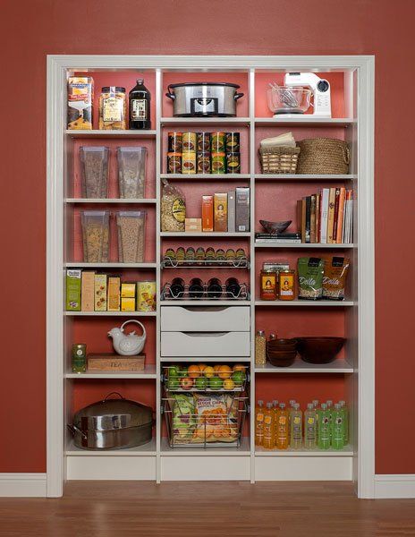 A pantry with a red wall and white shelves