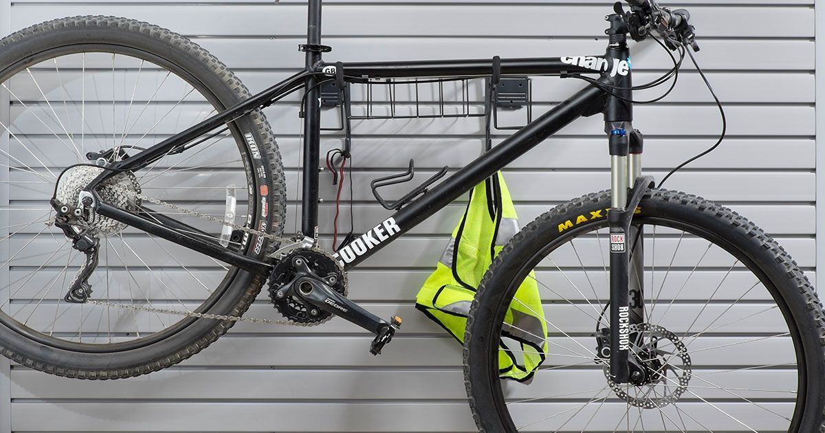 Black mountain bike hanging on a gray slat wall with a yellow safety vest.