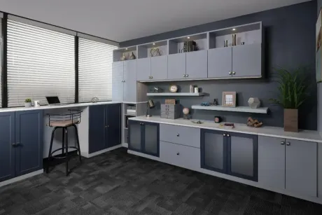 A modern home office with navy and light gray cabinets, open shelving, a desk workspace, and a dark carpeted floor.