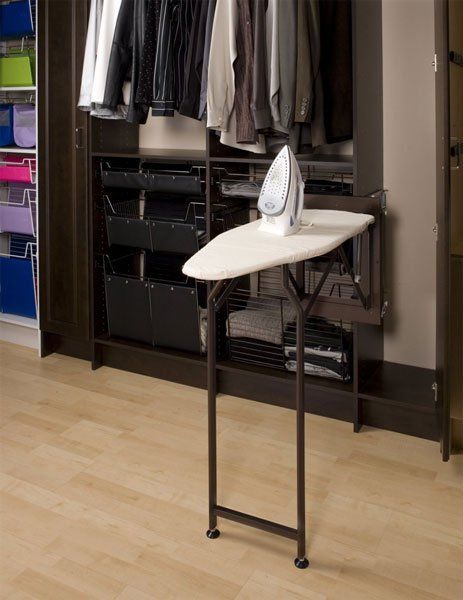 An ironing board in a closet with clothes hanging on it