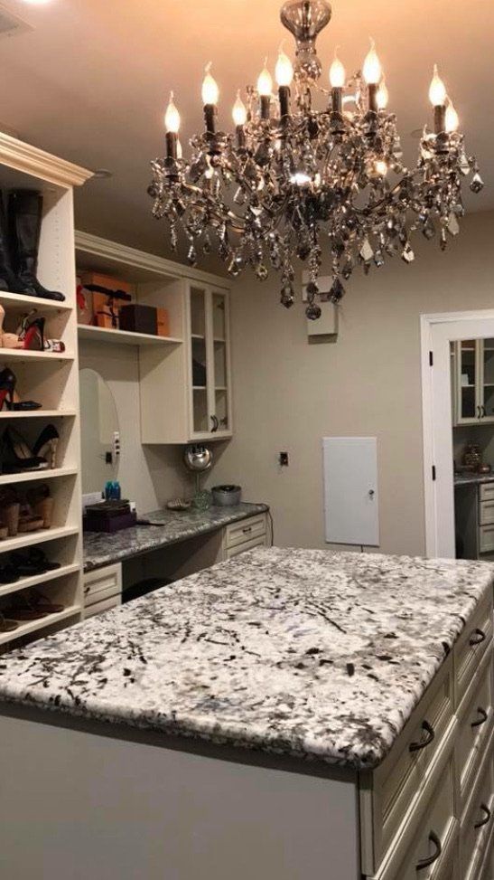 A walk in closet with a large island and a chandelier hanging from the ceiling.