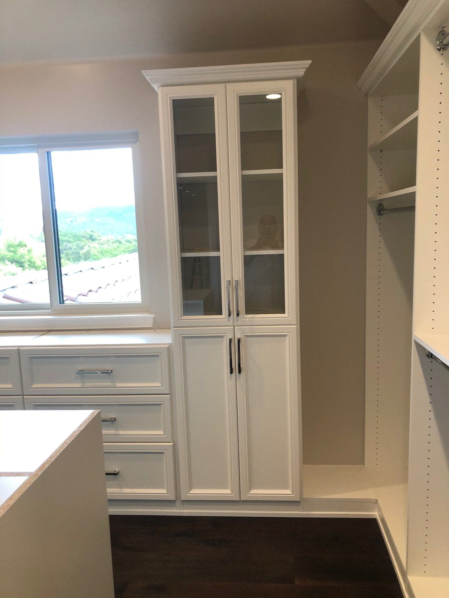 A walk in closet with white cabinets and a window