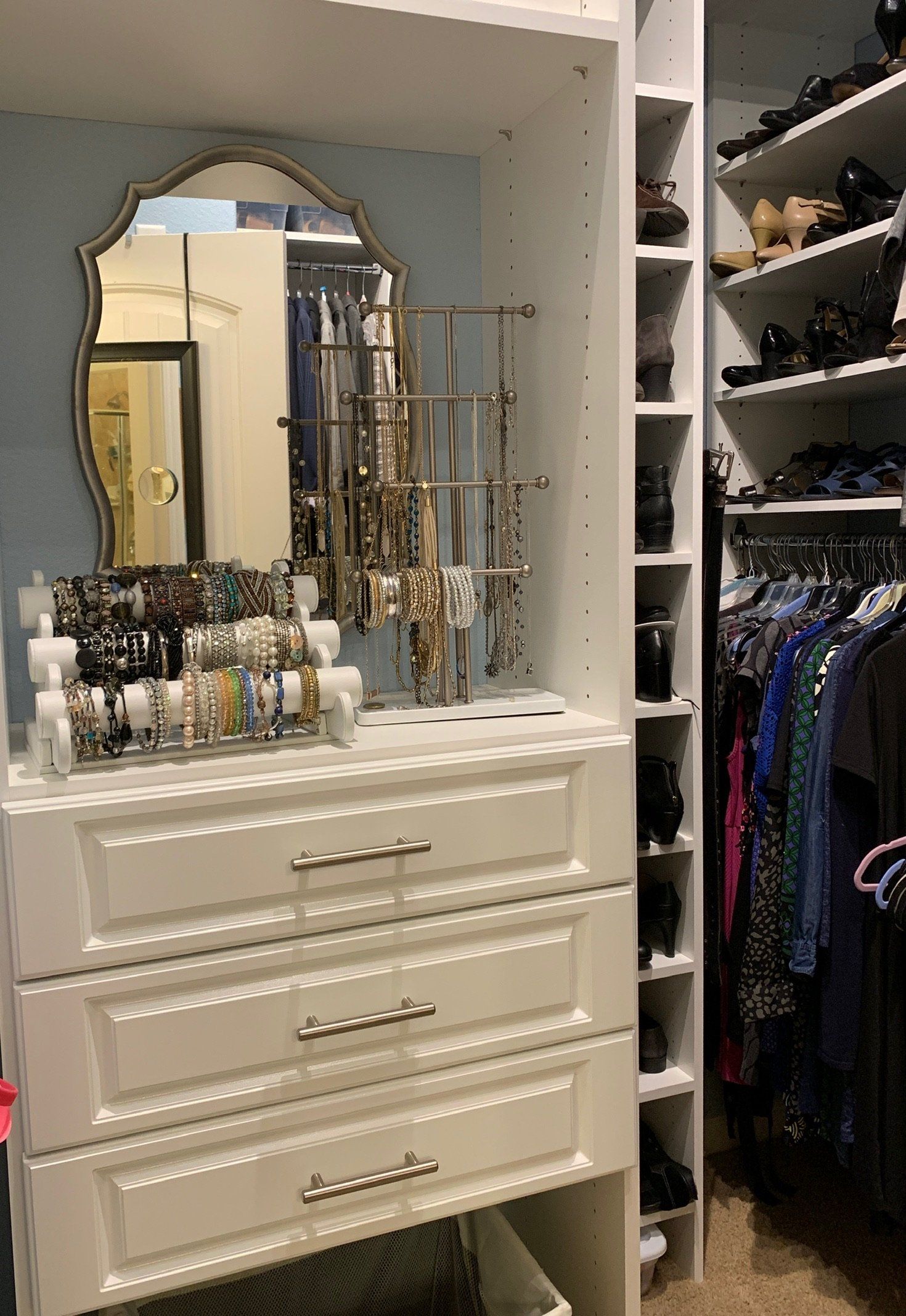 A closet with a dresser , mirror , and shelves filled with clothes.
