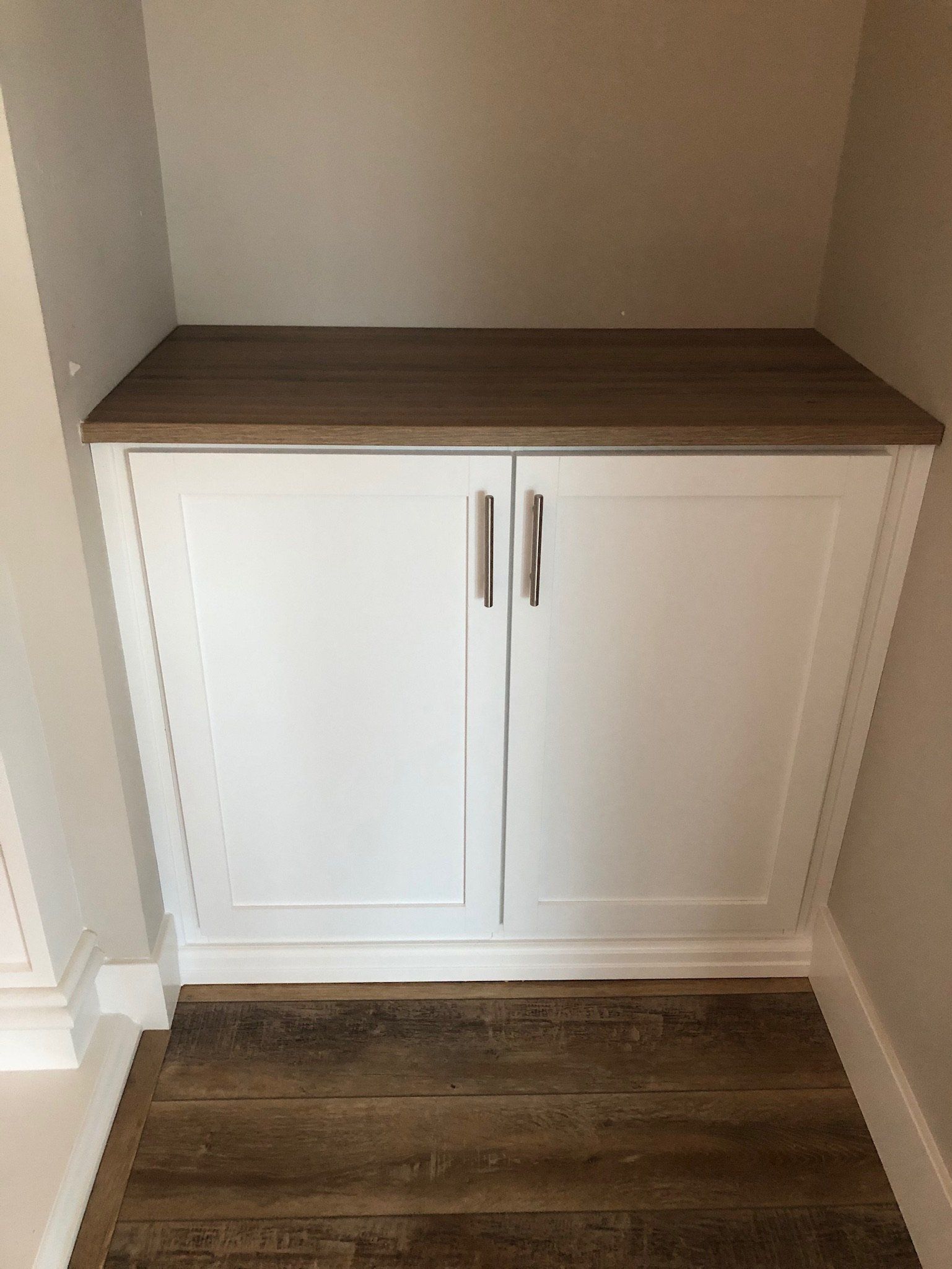 A white cabinet with a wooden top is in a corner of a room.