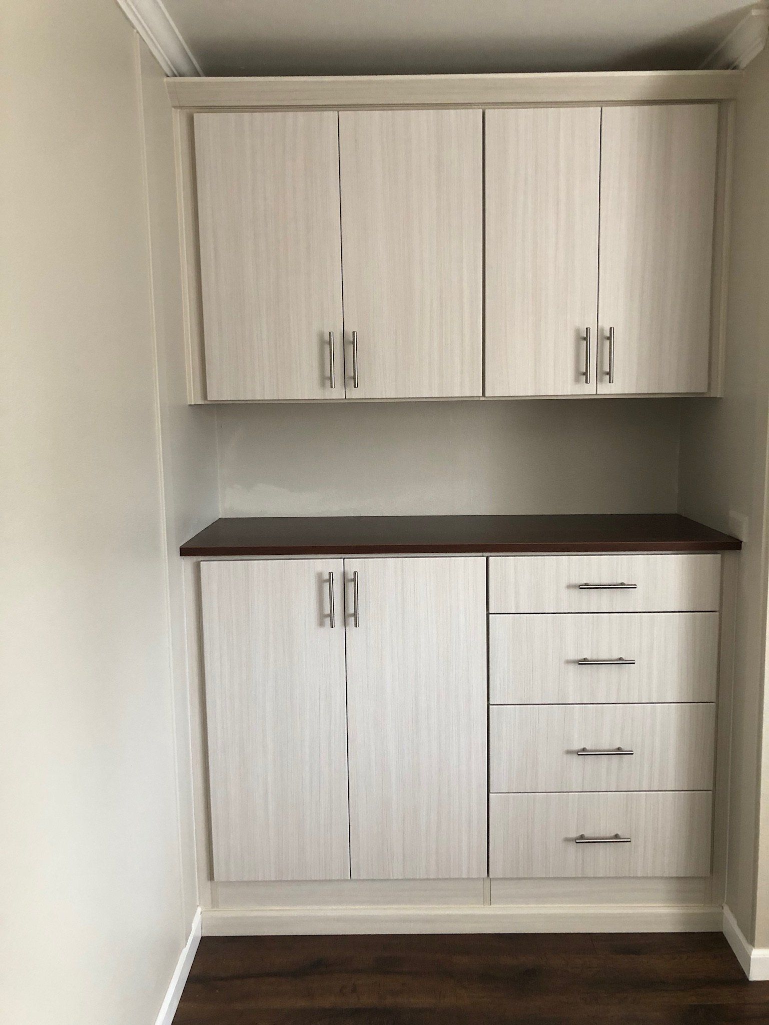 A room with white cabinets and drawers and a wooden floor.