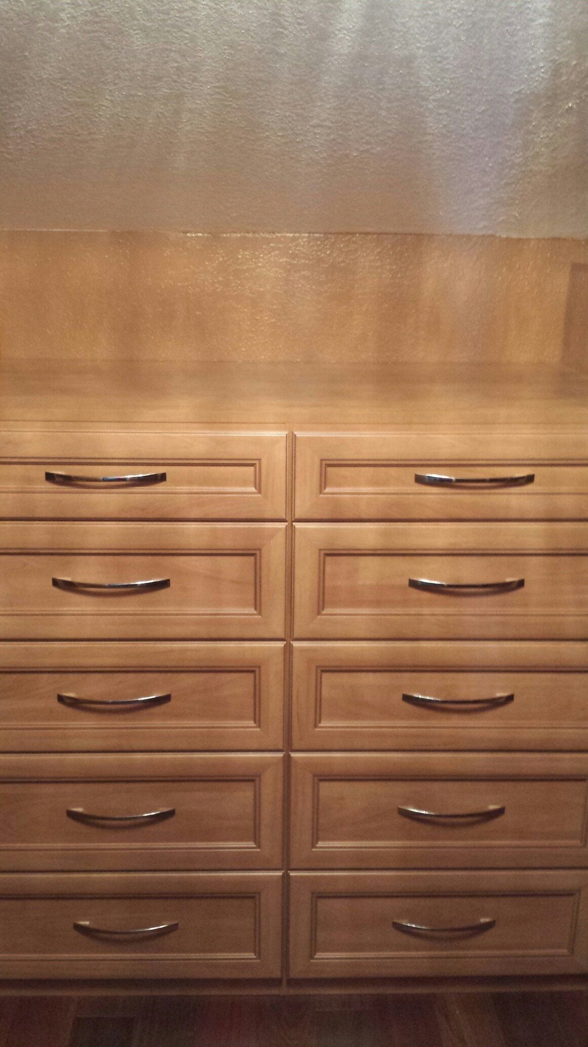 A wooden dresser with lots of drawers in a closet.