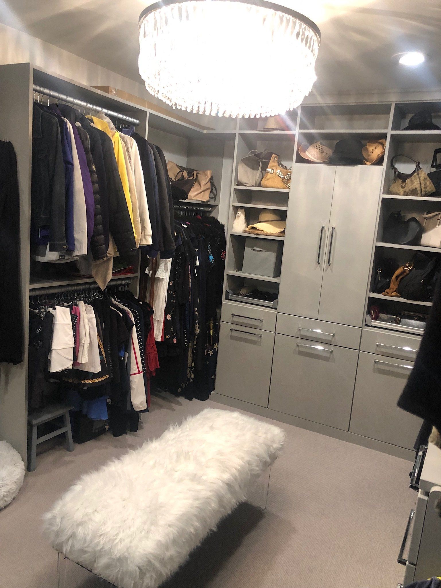 A walk in closet filled with lots of clothes and a white ottoman.