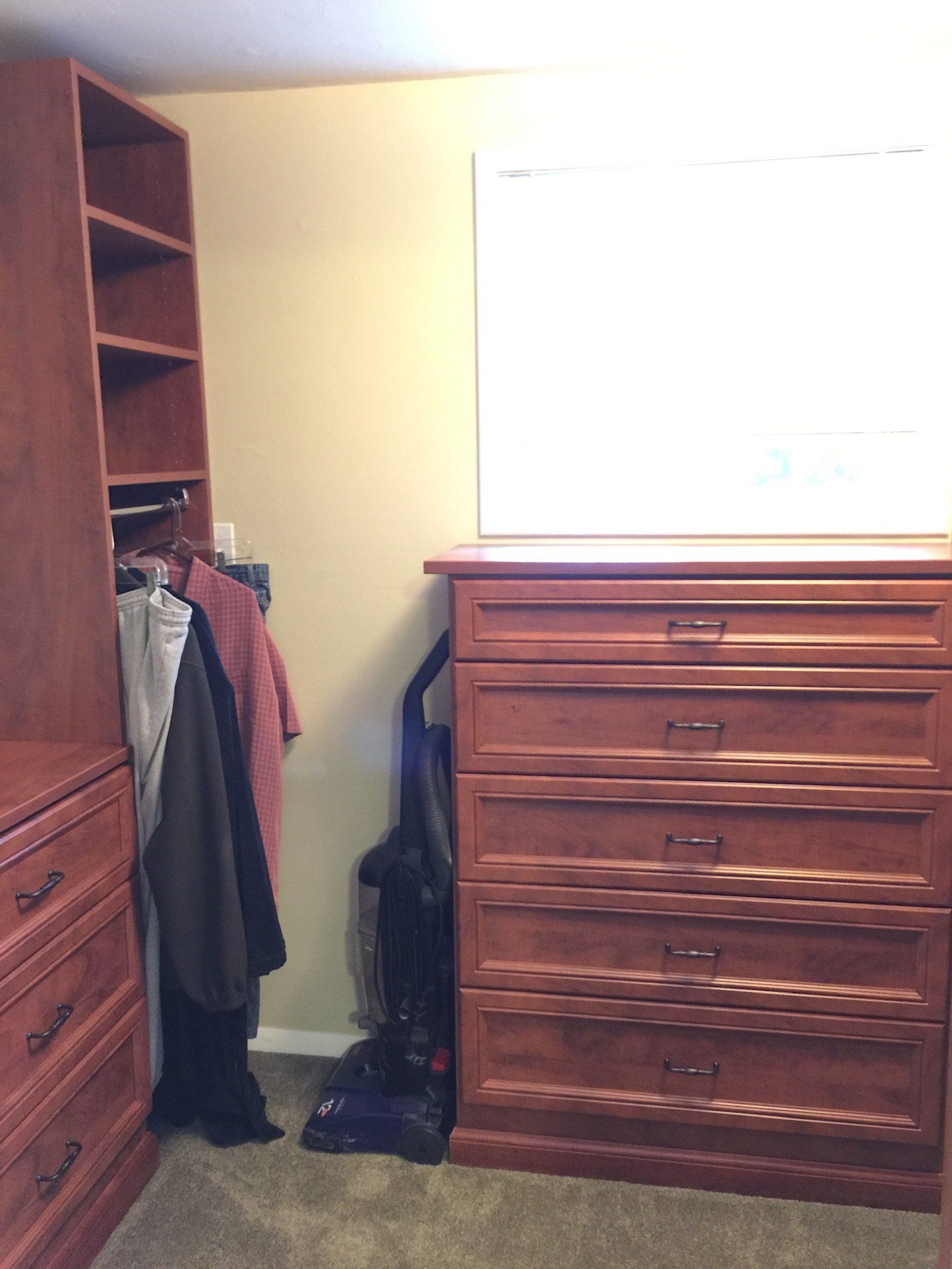 A walk in closet with wooden dressers , shelves , and a vacuum cleaner.