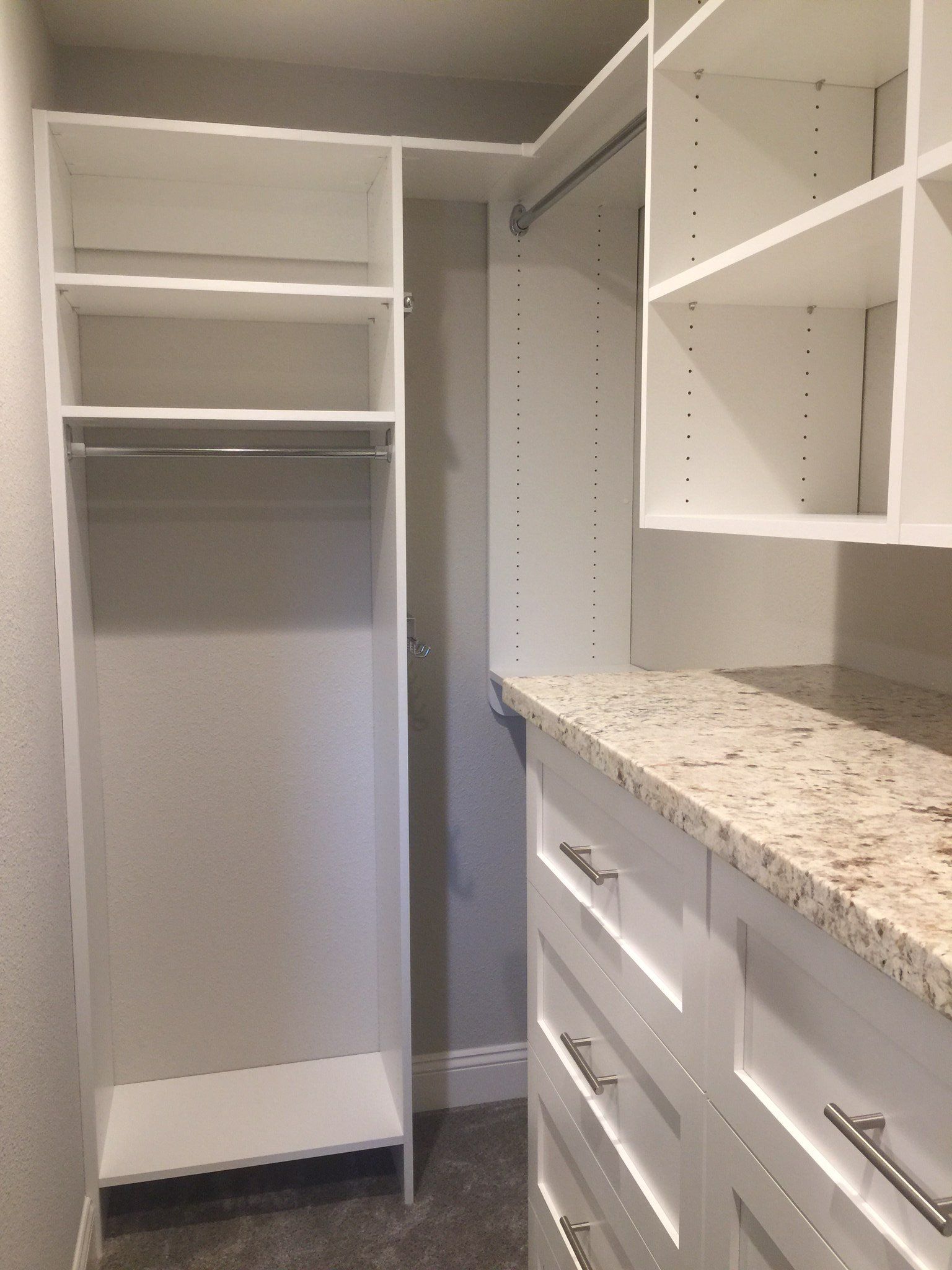 A walk in closet with white shelves and drawers and a granite counter top.