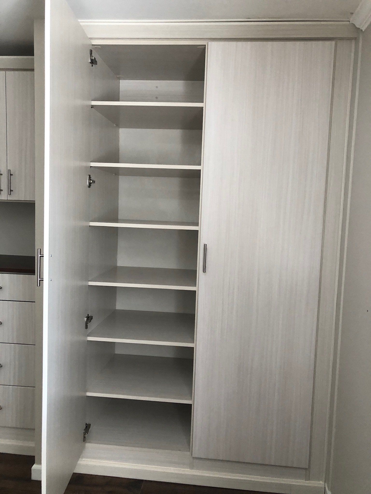 A white wardrobe with shelves and a door open in a room.