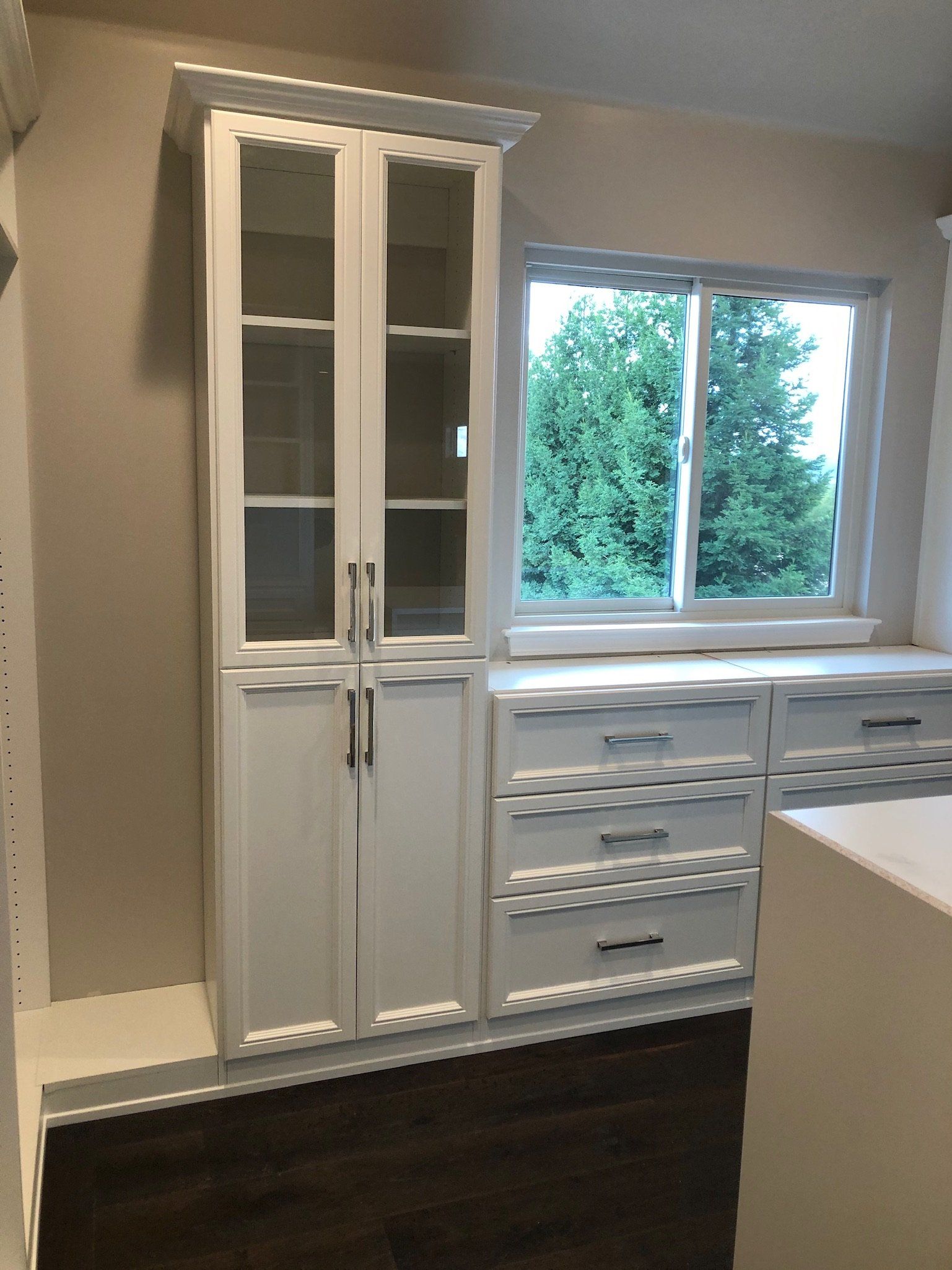 A room with white cabinets and drawers and a window