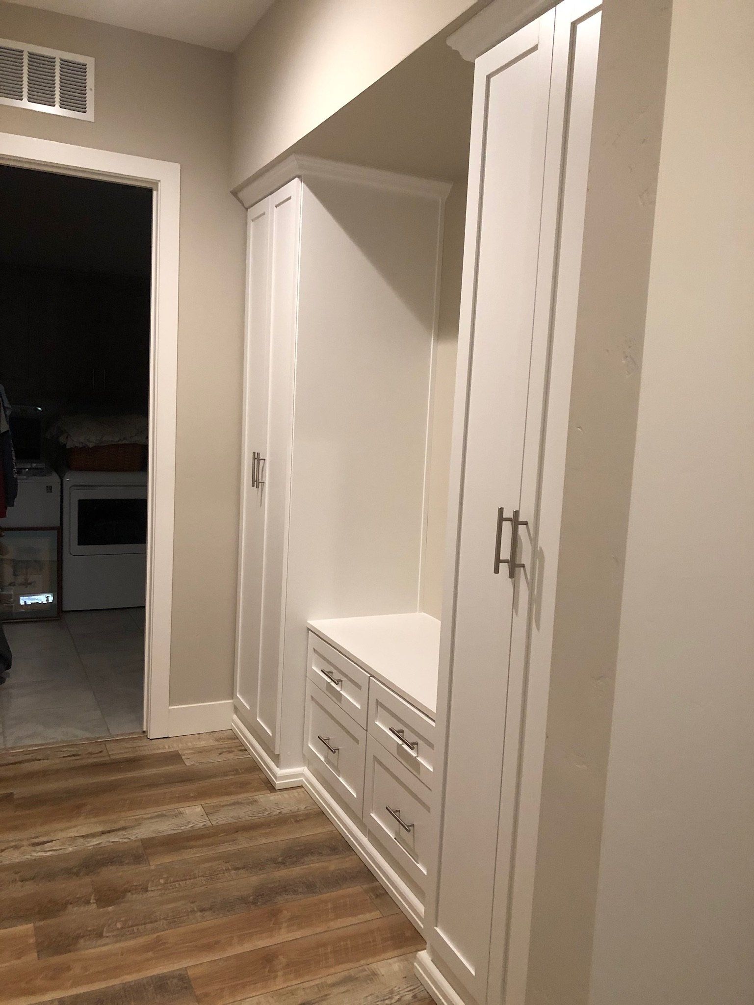 A hallway with white cabinets and a wooden floor