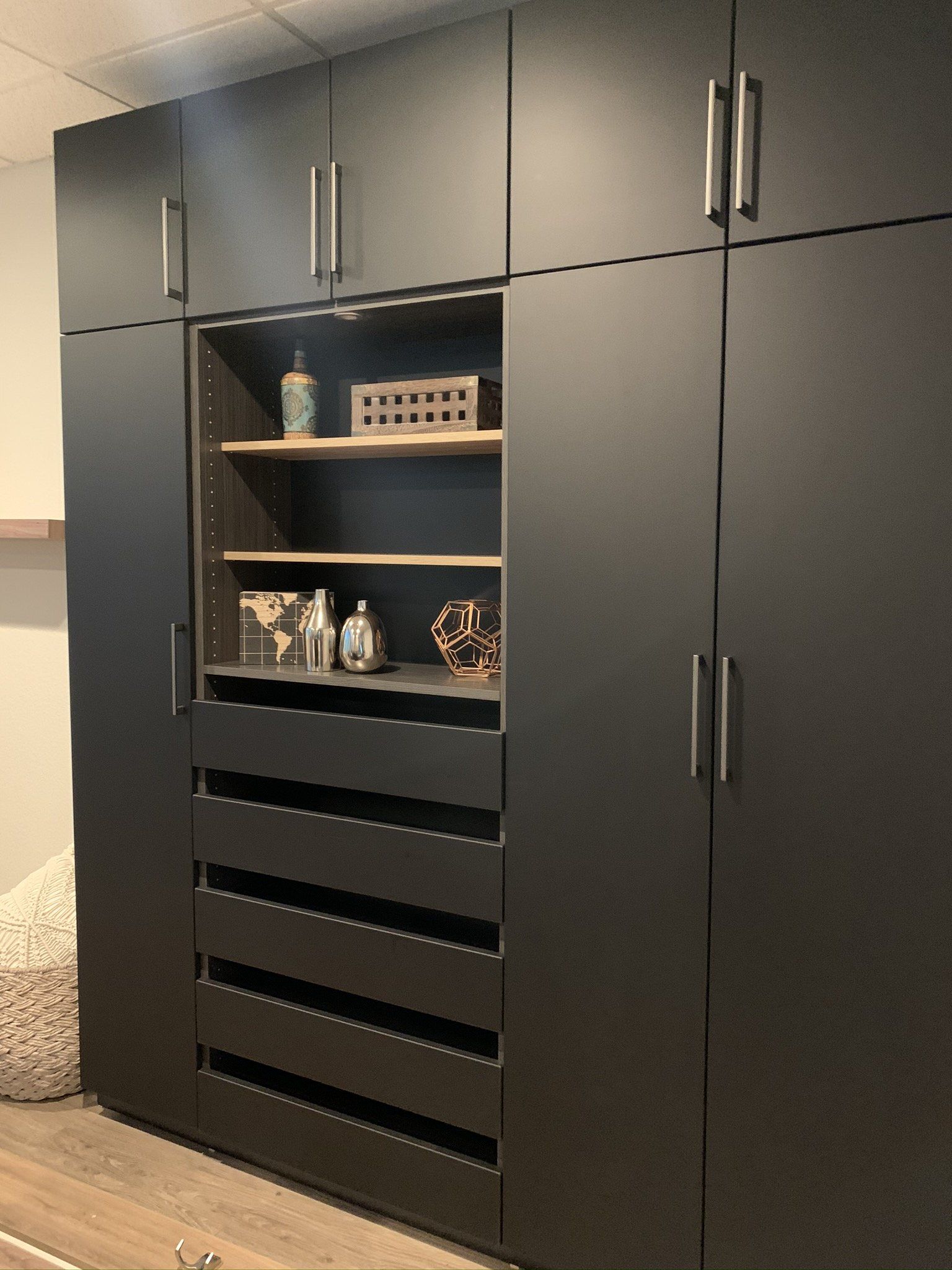 A large black wardrobe with drawers and shelves in a bedroom.