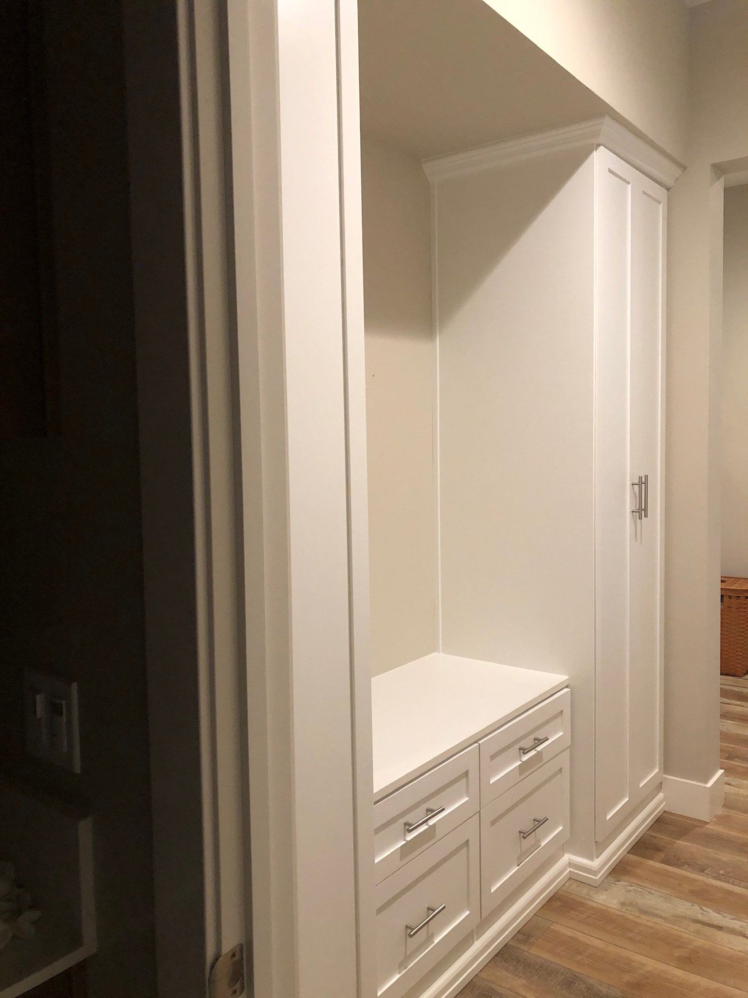 A hallway with white cabinets and drawers and a wooden floor.