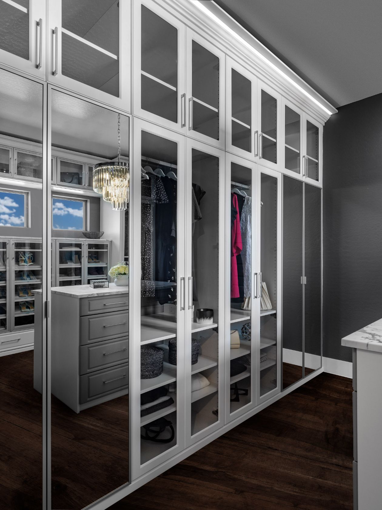A walk in closet with white cabinets and mirrored doors.