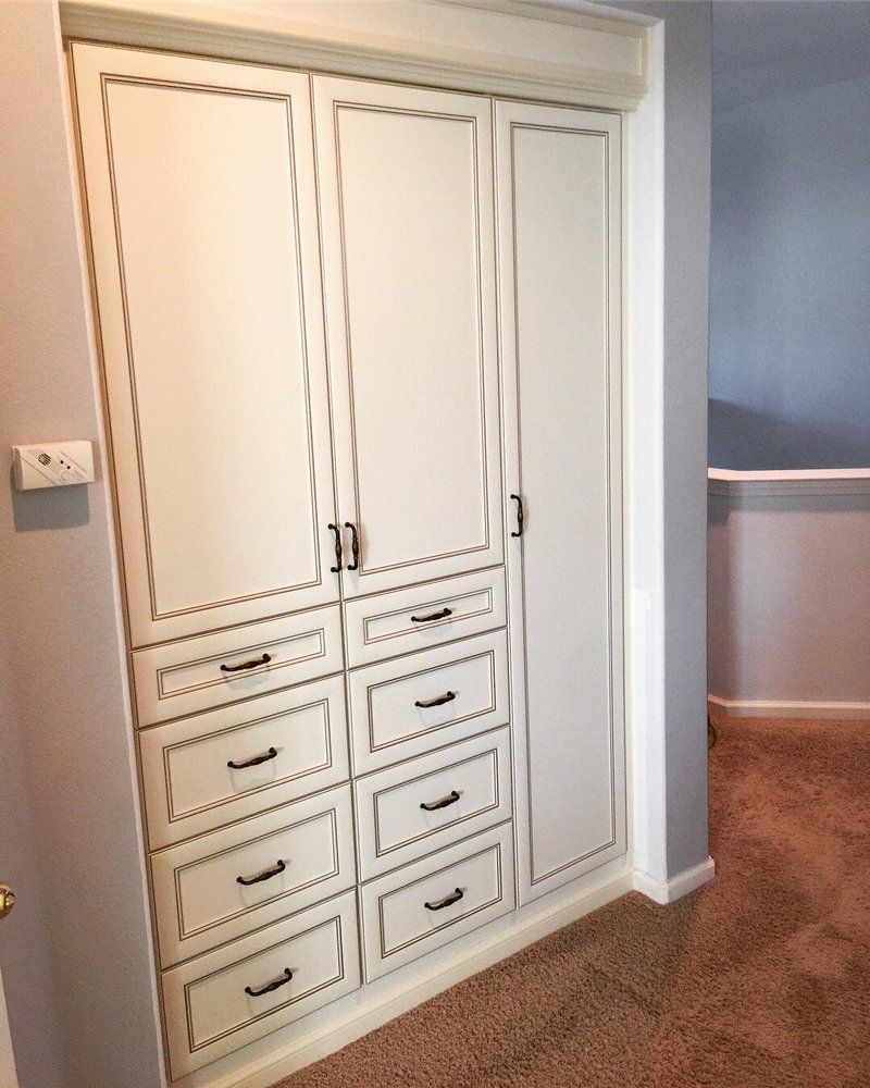 A closet with white cabinets and drawers in a room