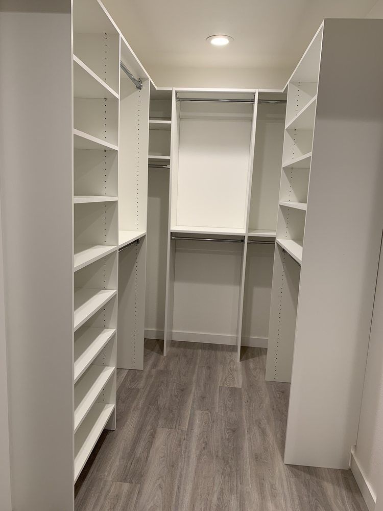 A walk in closet with white shelves and a wooden floor.