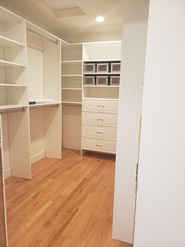 A walk in closet with hardwood floors and white shelves and drawers.