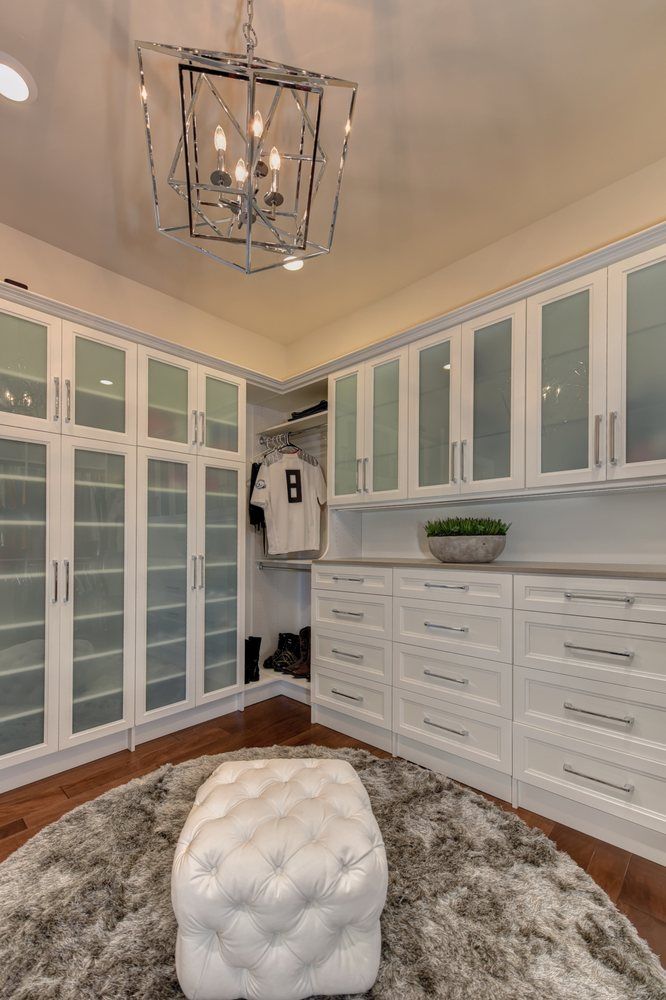 A walk in closet with white cabinets and glass doors.