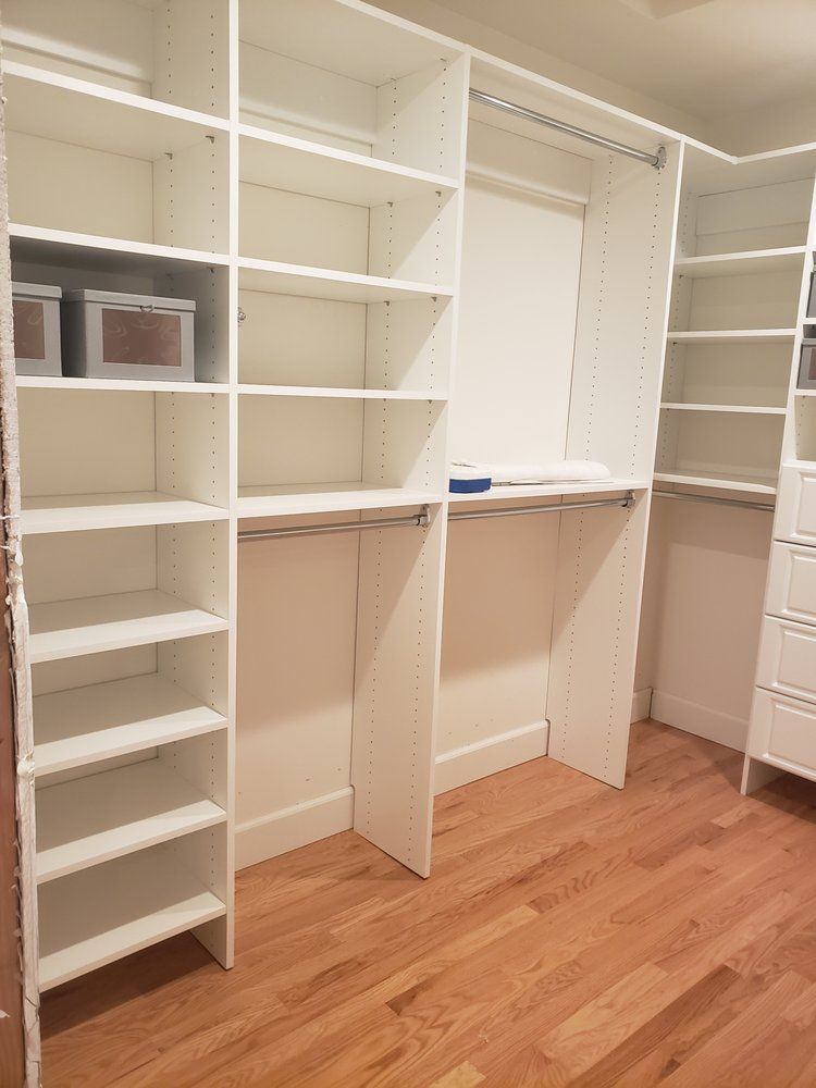 A walk in closet with wooden floors and white shelves.
