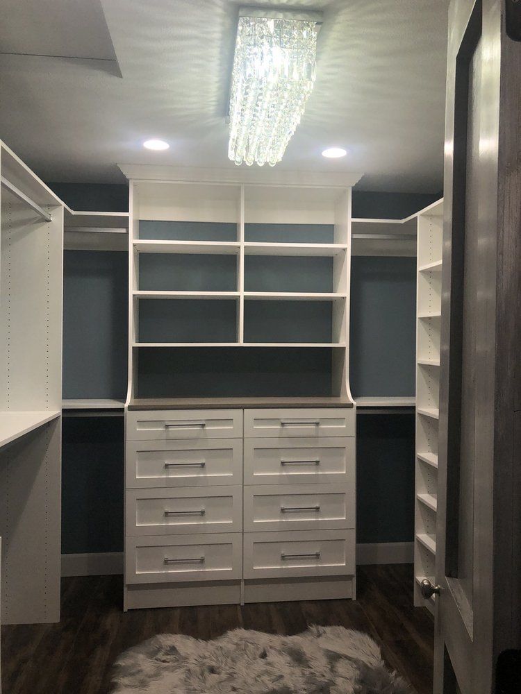 A walk in closet with lots of shelves and drawers and a chandelier hanging from the ceiling.