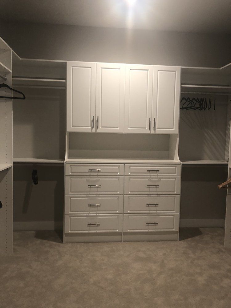 A walk in closet with white cabinets and drawers.