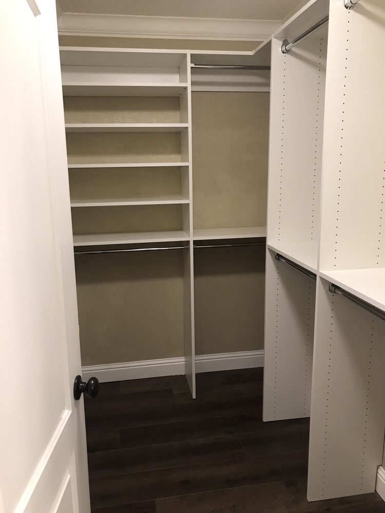 A walk in closet with white shelves and a wooden floor.