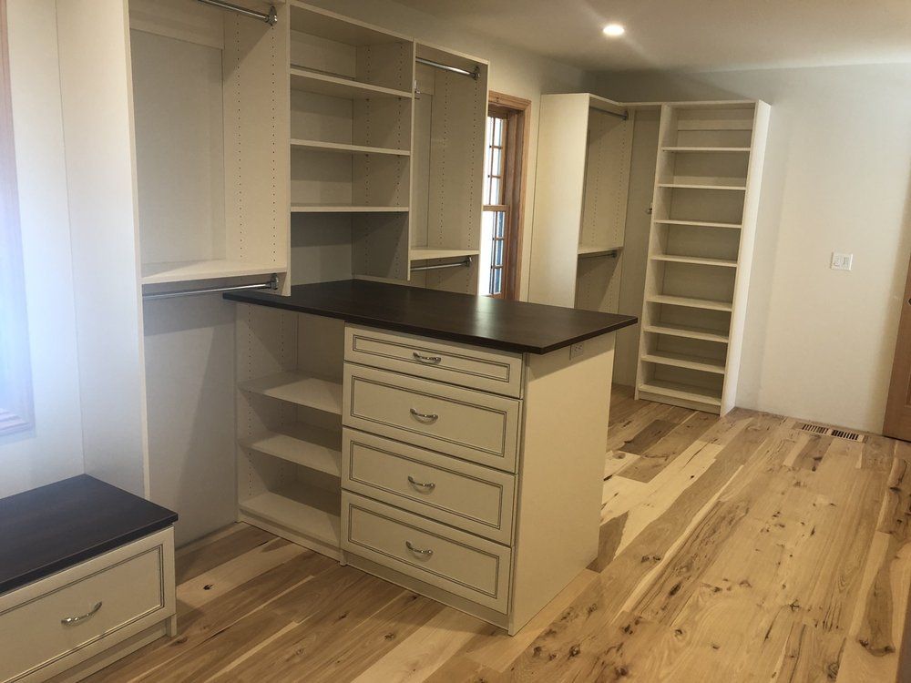 A walk in closet with lots of shelves and drawers and a large island in the middle.