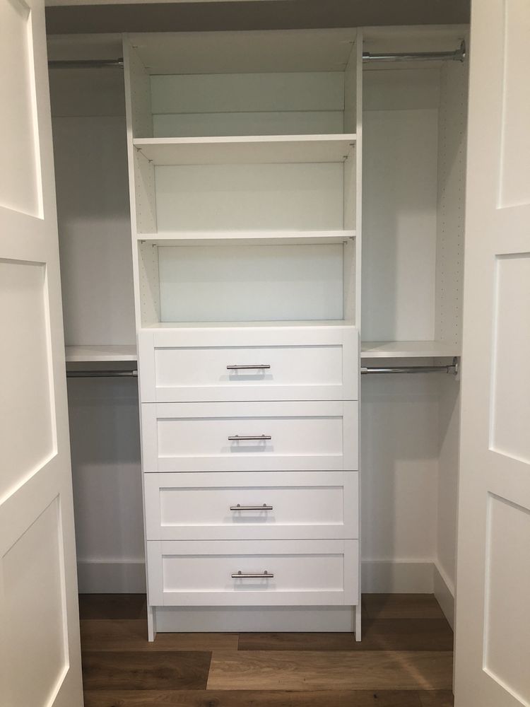 A walk in closet with white shelves and drawers.