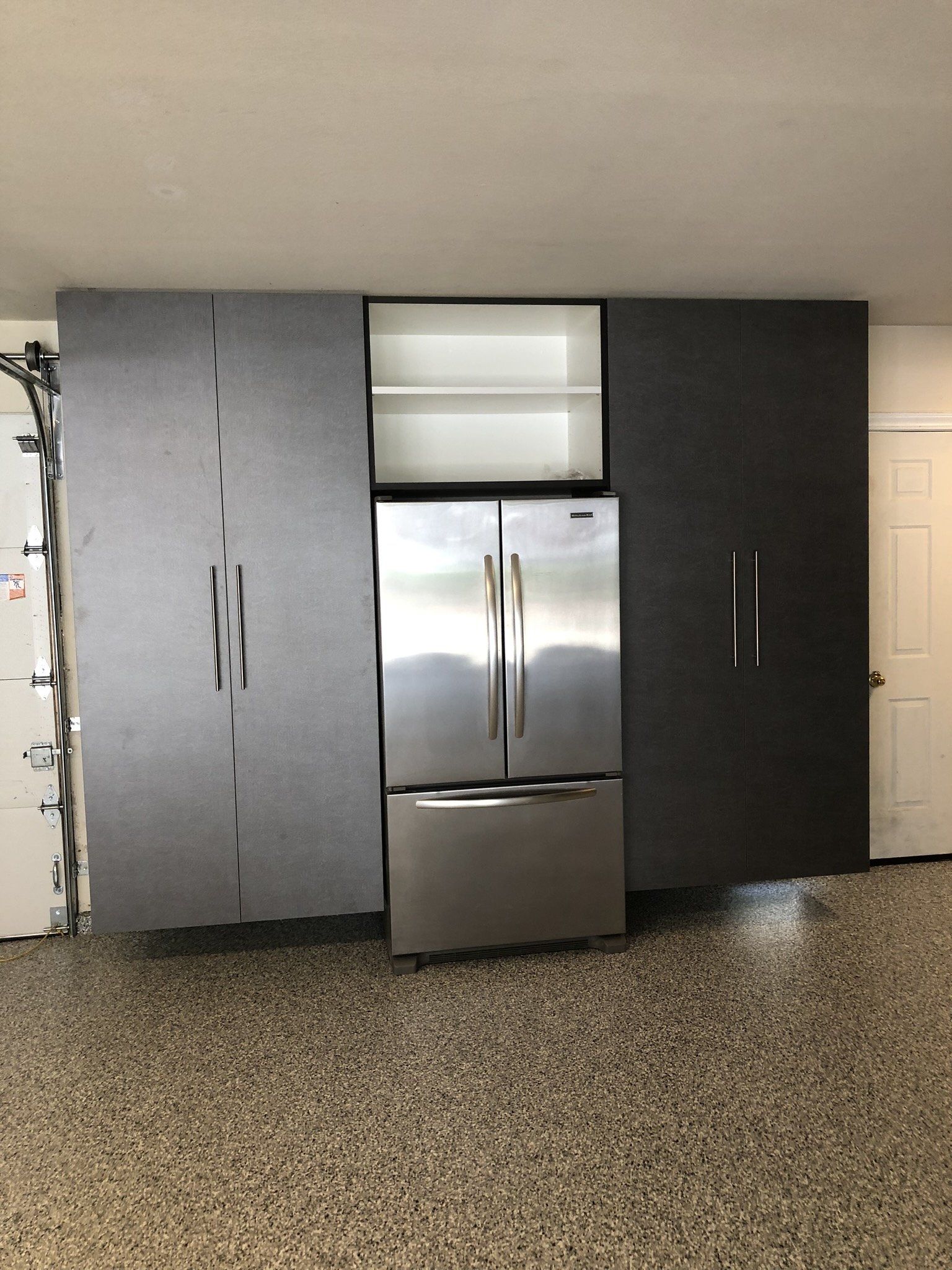 A stainless steel refrigerator is built into a wall in a garage.